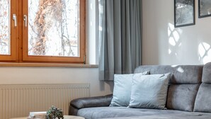 A modern living room with a grey sofa, a round wooden coffee table, and a window with curtains. - Cosy apartment in the center with a garden (Kirchberg in Tirol)