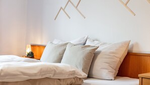 A neatly made bed with white linens and multiple pillows, a wooden headboard, and a wall-mounted light fixture. - Cosy apartment in the center with a garden (Kirchberg in Tirol)