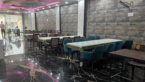 Restaurante com chão de mármore, mesas com toalhas verdes e cadeiras azuis.