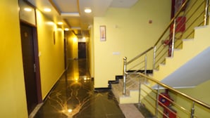Corredor de hotel com chão de mármore, paredes amarelas e escada com grades de metal.