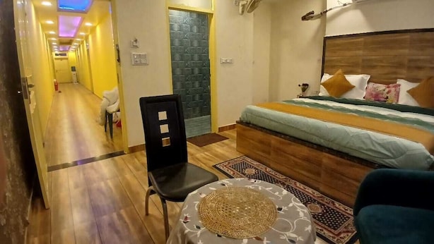 Quarto de hotel com uma cama, uma cadeira, uma mesinha e uma porta que dá para outro cômodo.