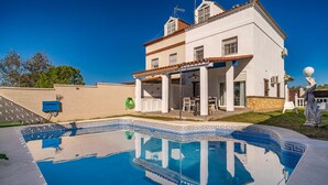 Une maison à deux étages avec une piscine, une terrasse dotée de mobilier d’extérieur et un mur en pierre.