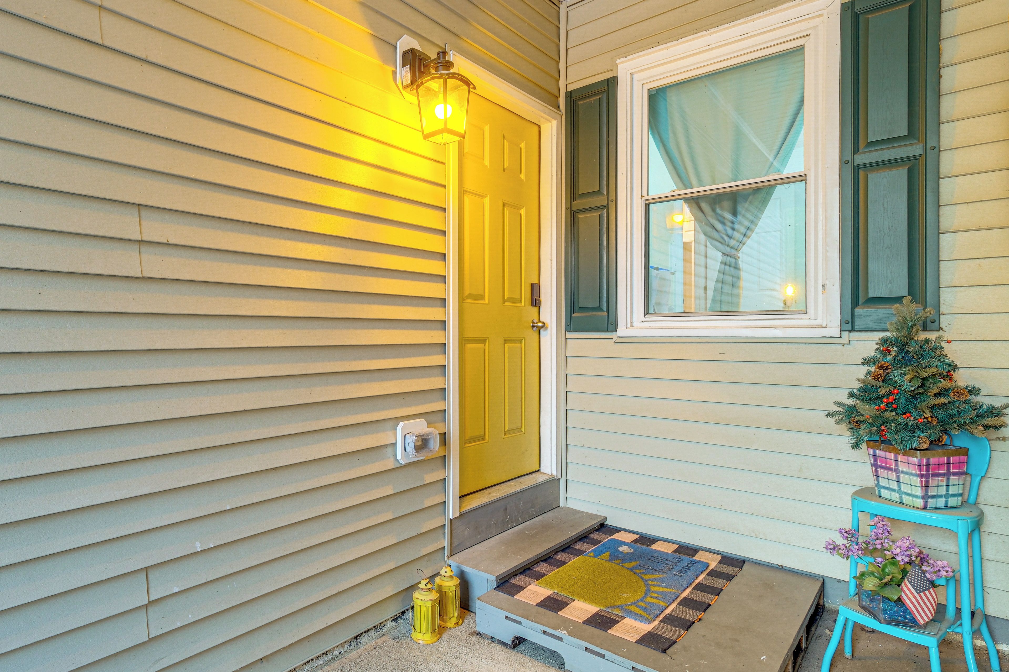 A house entrance with a yellow door, a small Christmas tree, and a welcome mat.