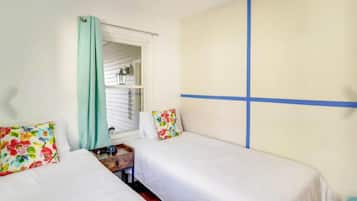 A room with two beds, a window with curtains, a small table, and a wall with a blue stripe.