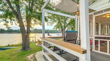 A covered deck with outdoor seating, overlooking a lake.