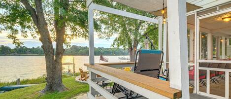 A covered deck with outdoor seating, overlooking a lake.
