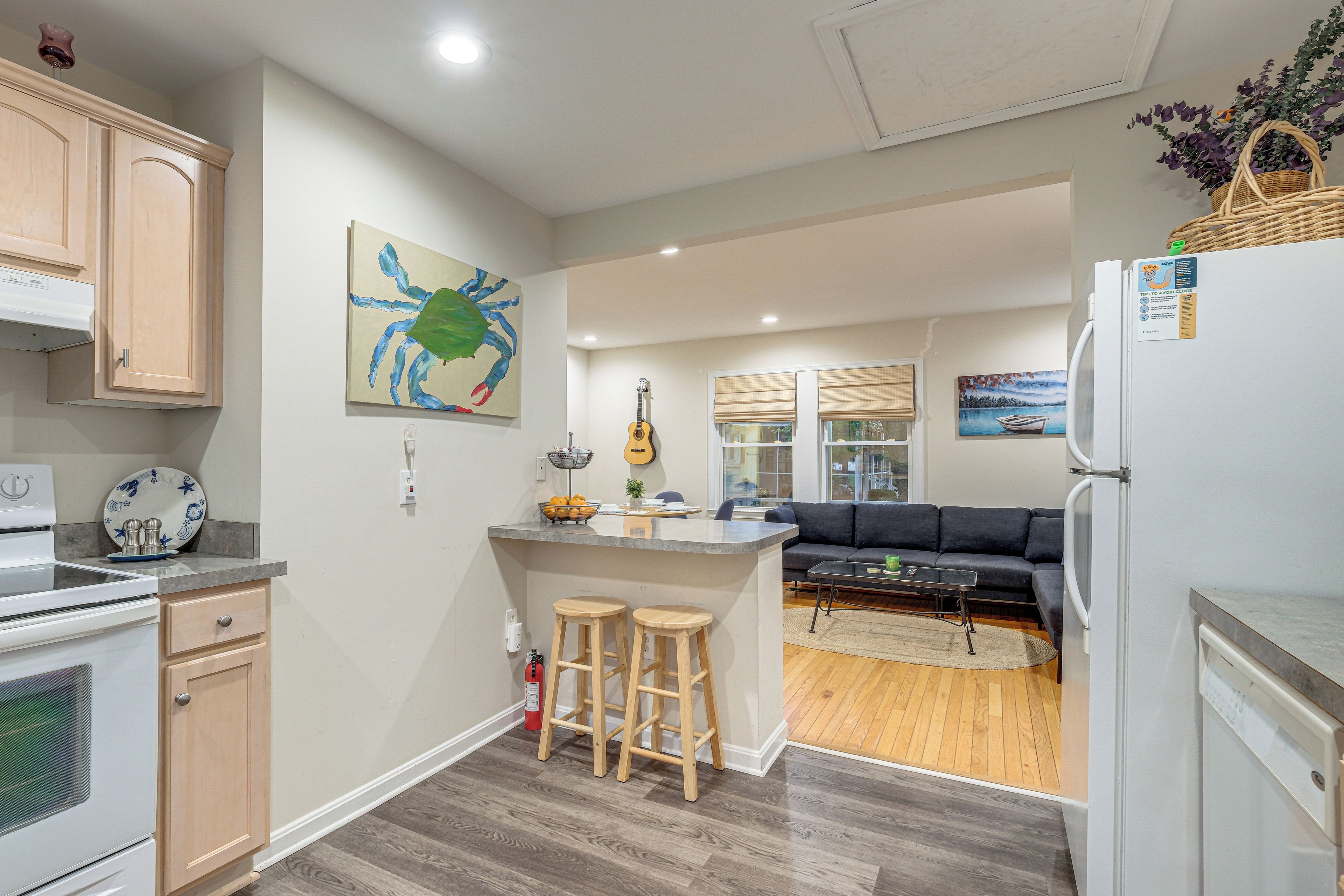A modern kitchen with wooden cabinets, a dining area with a dark sofa, and a living room with a wooden floor.