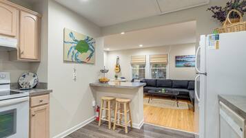 A modern kitchen with wooden cabinets, a dining area with a dark sofa, and a living room with a wooden floor.
