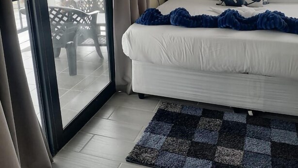 Una camera da letto con un letto, una finestra con tende e una vista del balcone esterno, oltre a un tappeto a scacchi.