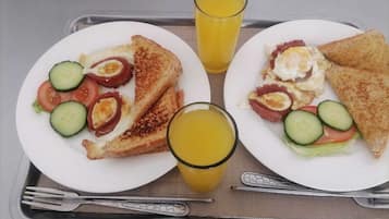 Un plateau avec deux assiettes de petit-déjeuner, chacune contenant des toasts, des œufs, du bacon, des tomates et des concombres, ainsi que deux verres de jus d’orange.