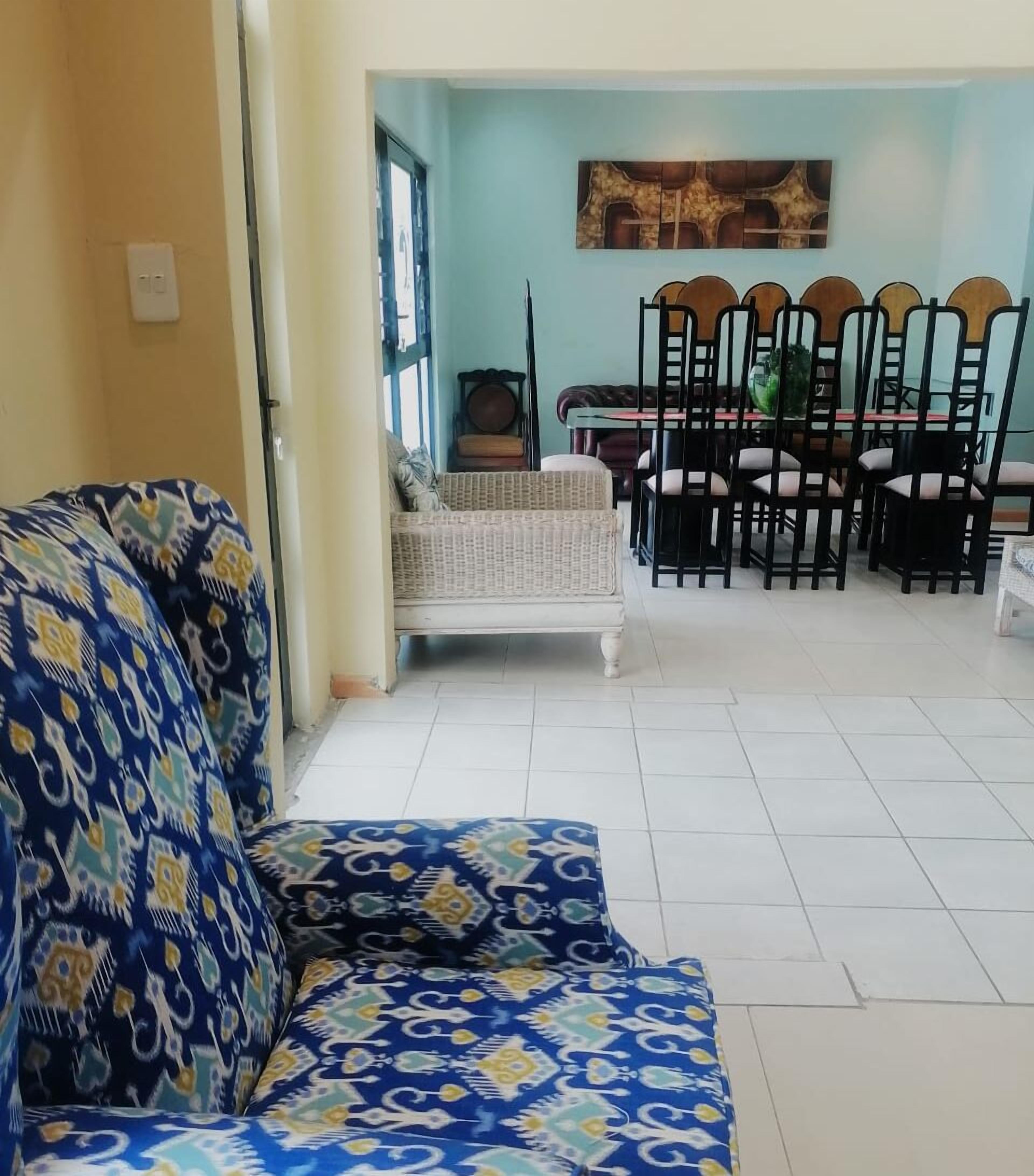 A living room with a patterned sofa, a dining table with chairs, and a light blue wall.