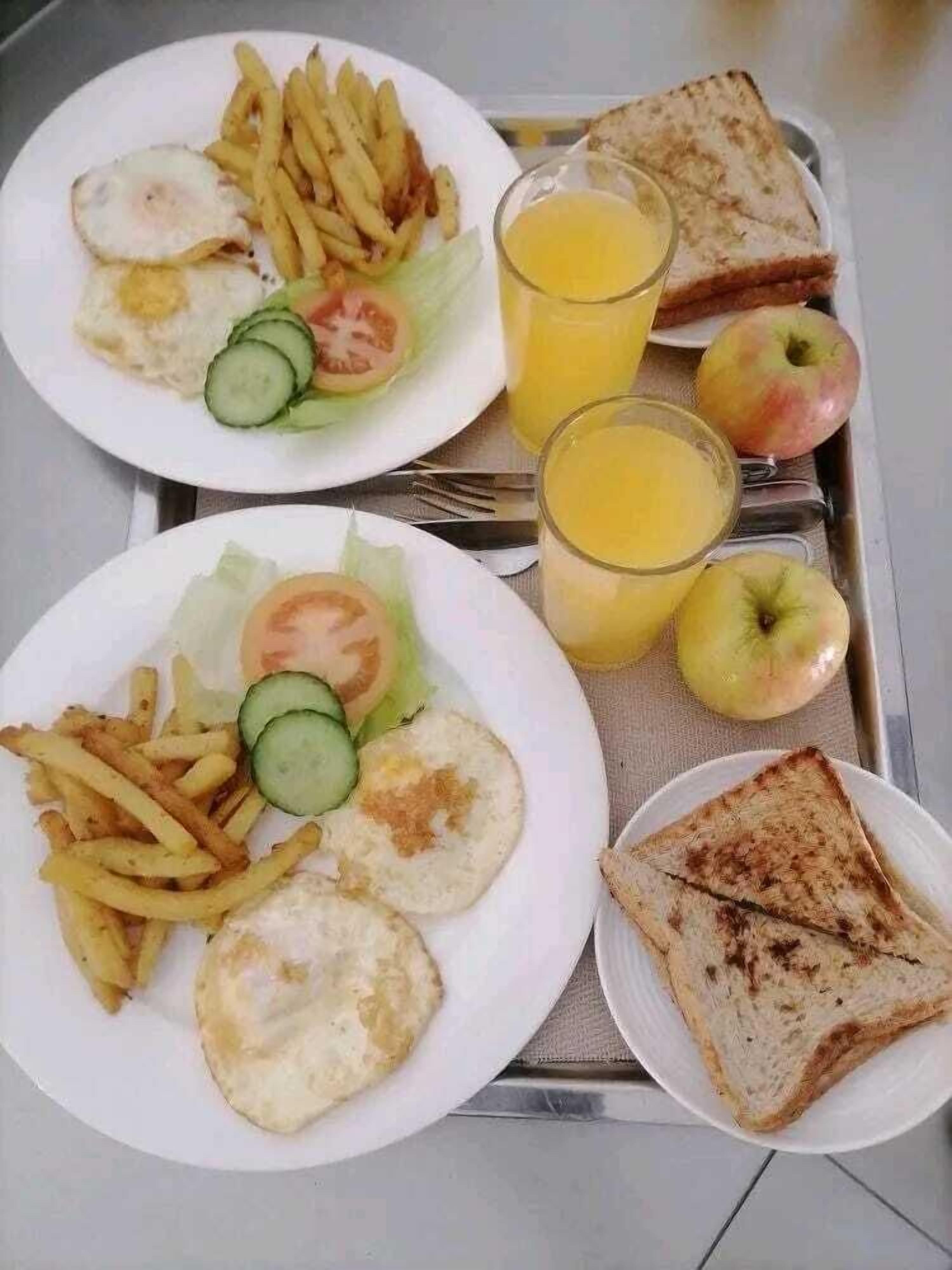 A tray with two plates of food, including eggs, fries, and toast, along with two glasses of orange juice and two apples.