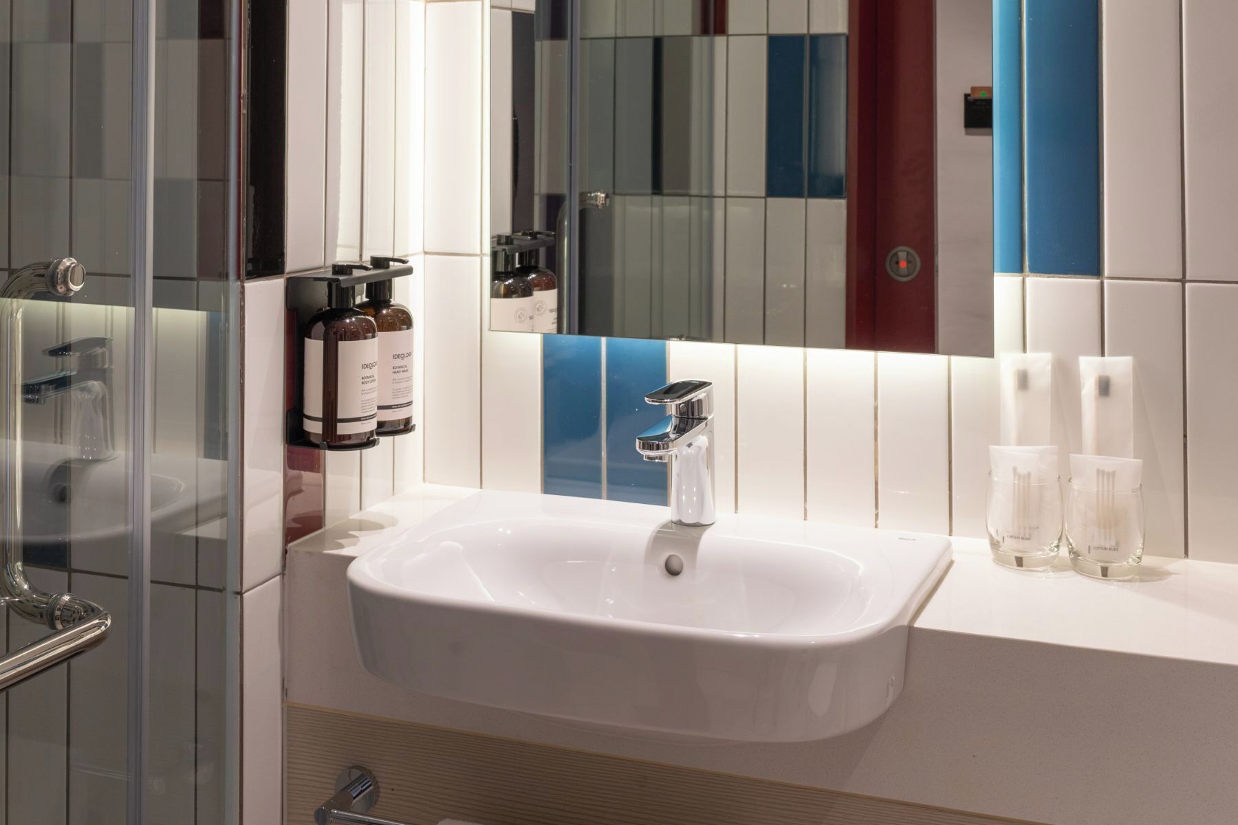 A bathroom with a white sink, chrome faucet, and a mirror. There are toiletries on the counter.