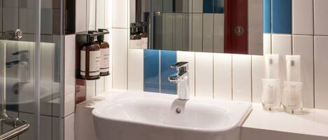 A modern bathroom with a white sink, glass shower enclosure, and a mirror reflecting a colorful wall.