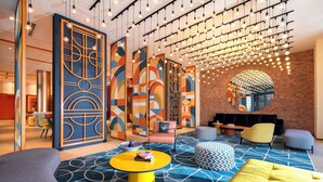A modern lounge area with geometric patterned walls, a round mirror, and a variety of seating options including a yellow sofa and ottoman. - lyf Georgetown Penang (George Town)