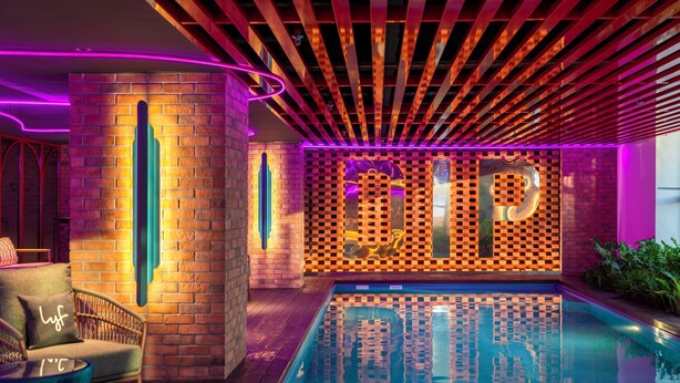 A modern indoor pool area with a brick wall, a lounge chair, and a pool with a checkered pattern. - lyf Georgetown Penang (George Town)