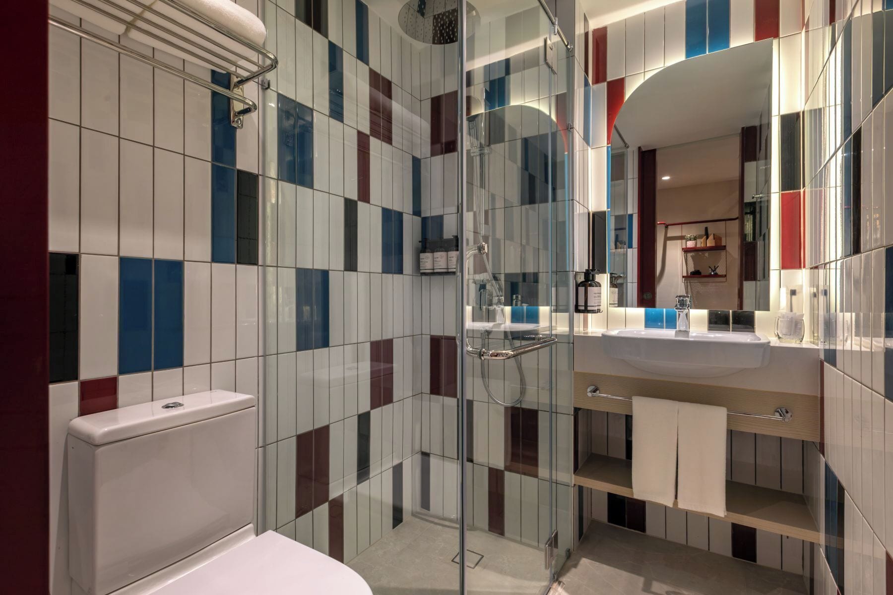 A modern bathroom with a glass shower enclosure, a white sink, and a mirror with a red frame.