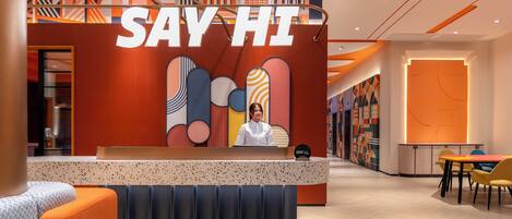 A reception area with a 'SAY HI' sign, a receptionist, a counter, and a seating area with a table and chairs.