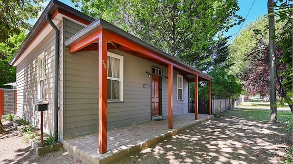 Charming single-story home with a gabled roof and covered porch, set amidst a well-manicured lawn and lush trees.