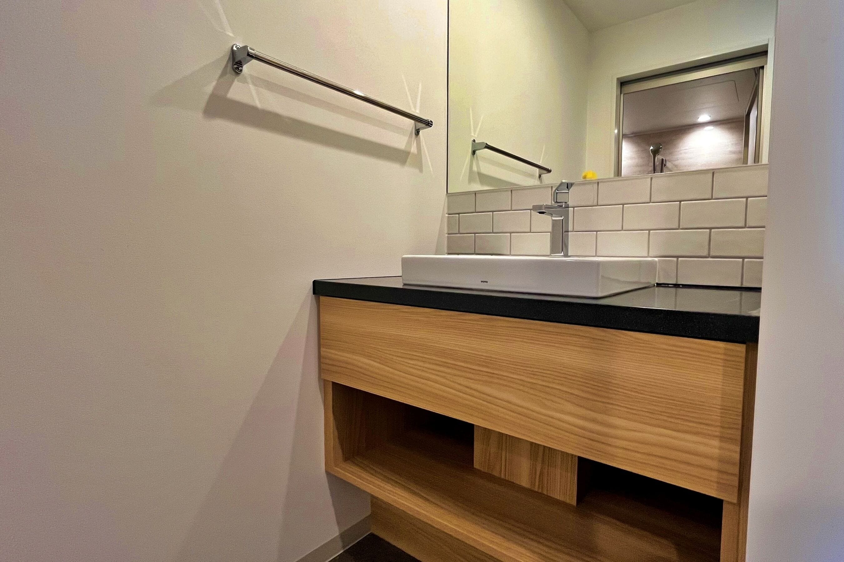 A modern bathroom with a white sink, black countertop, and wooden vanity.