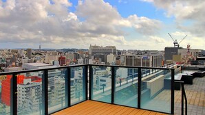 A rooftop terrace with a city view, glass railings, and a wooden floor. - La'gent Hotel Okinawa Naha (Naha)