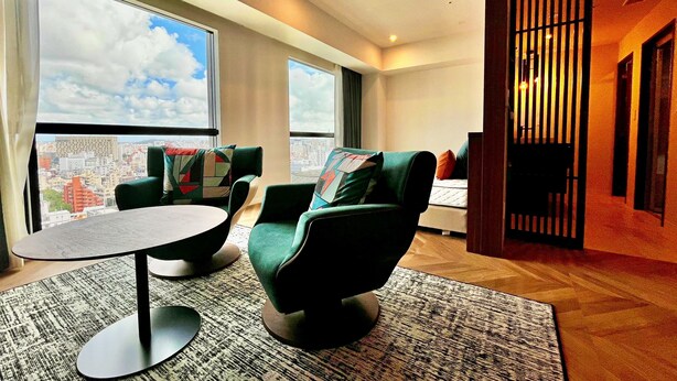 A modern hotel room with a large window offering a city view, a round table, and two green armchairs. - La'gent Hotel Okinawa Naha (Naha)