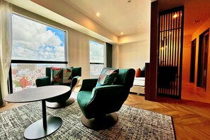 A modern hotel room with a large window offering a city view, a round table, and two green armchairs. - La'gent Hotel Okinawa Naha (Naha)