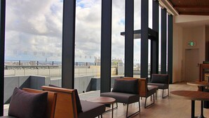 A modern lounge area with high ceilings and large windows, offering views of the cityscape and a body of water. - La'gent Hotel Okinawa Naha (Naha)