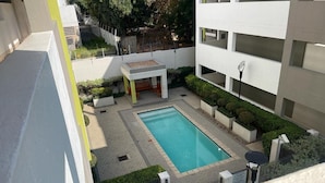 Un bâtiment moderne doté d’une piscine rectangulaire, entourée d’une zone pavée et de verdure.