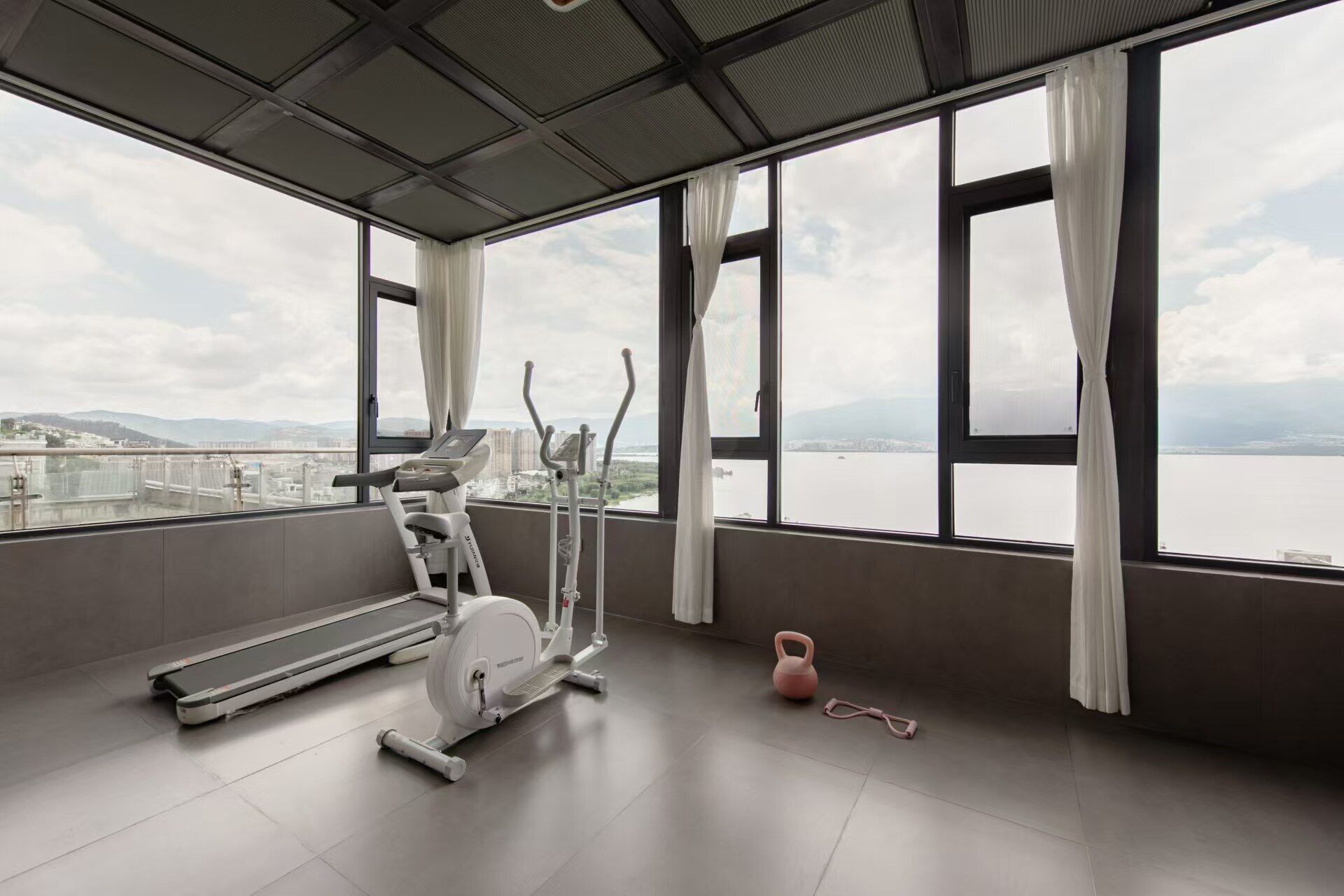A gym with exercise equipment, large windows, and a view of a body of water and cityscape.