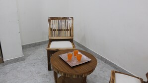 A corner room with a wooden chair and a small round table with a tray holding three glasses of orange juice. - Hotel Castle Grand (New Delhi)