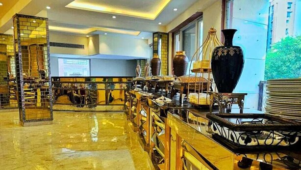 A spacious hotel lobby with a marble floor, a central bar area with a large black vase, and a view of a building through the window. - Hotel Castle Grand (New Delhi)