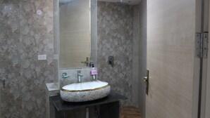 A bathroom with a round sink, a mirror, and a shower area. - Hotel Castle Grand (New Delhi)