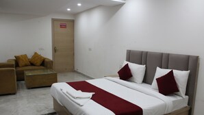 A hotel room with a bed, a sofa, a glass coffee table, and a door. - Hotel Castle Grand (New Delhi)