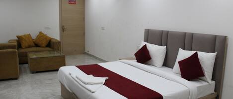A hotel room with a bed, a sofa, a glass coffee table, and a door.
