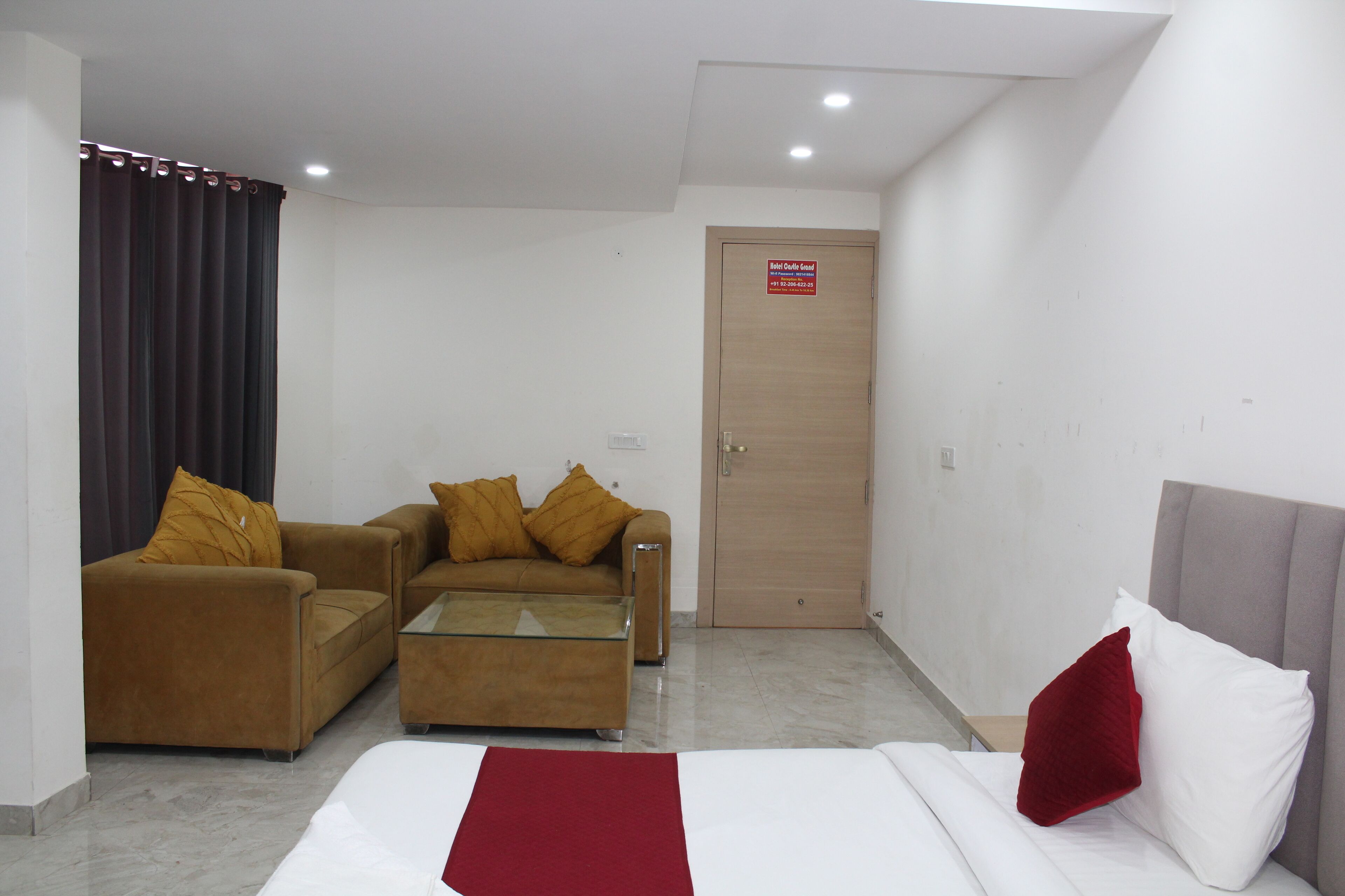 A hotel room with a bed, a sofa, a coffee table, and a door with a sign.