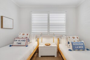 Ein Zimmer mit zwei Betten, einem kleinen Tisch und einem Fenster mit Jalousien.