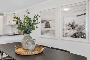 A dining area with a dark wooden table, a striped vase with green foliage, and two framed black and white landscape paintings on the wall.