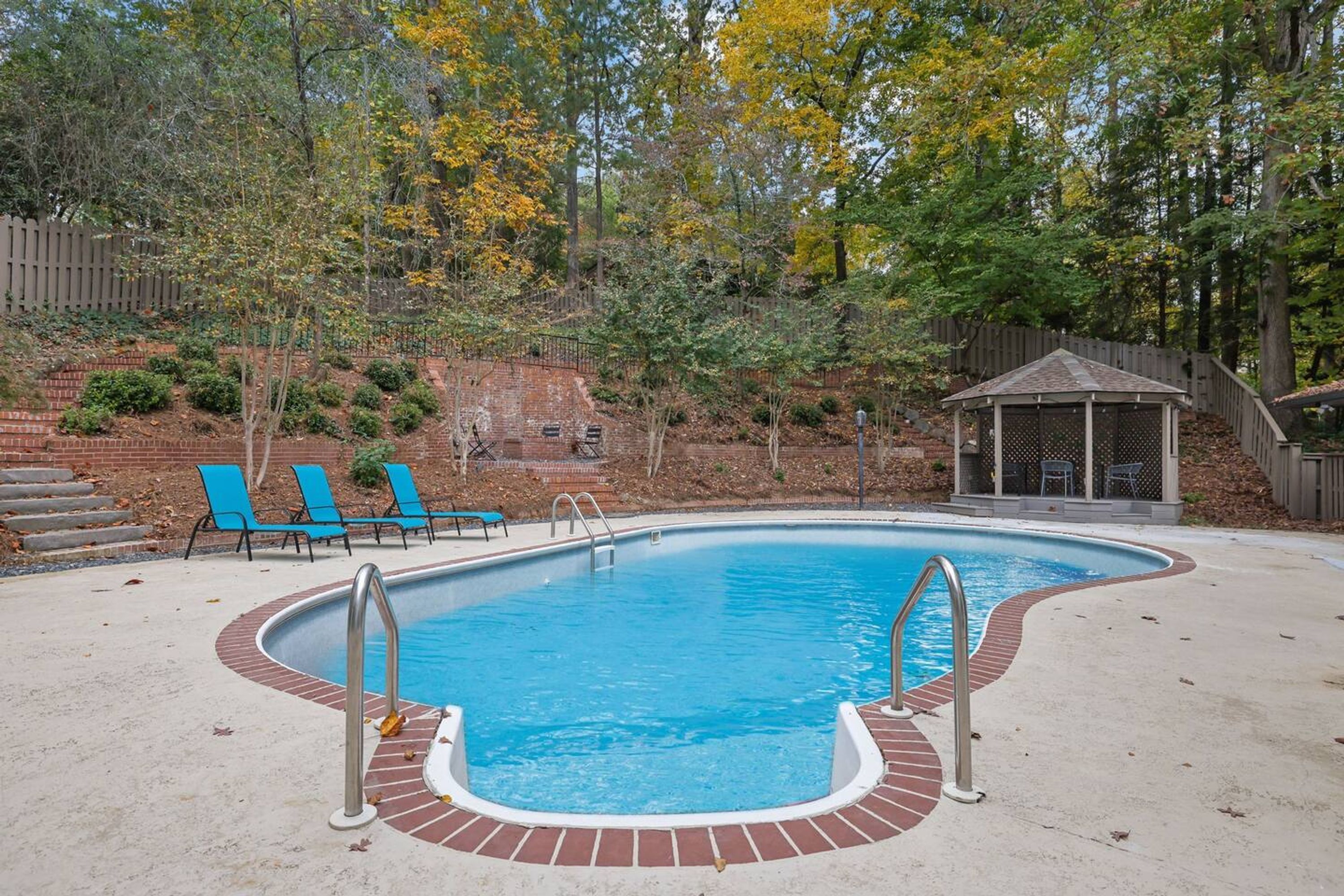 A swimming pool with a brick border, surrounded by a wooden deck and blue chairs.