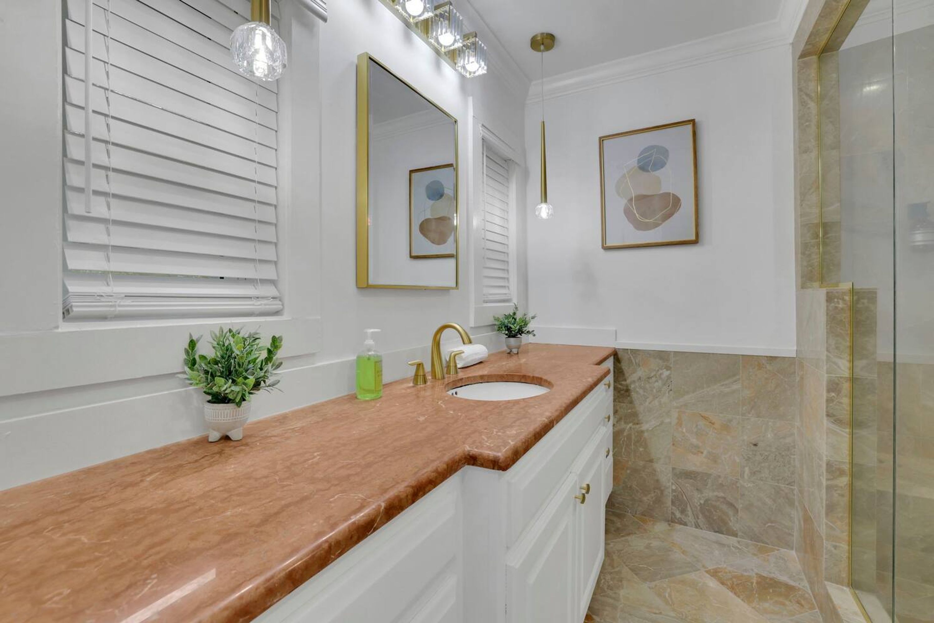 A bathroom with a marble countertop, a sink, a mirror, and a shower area.