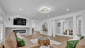 A spacious living room with a large flat-screen TV, a wooden coffee table, and a comfortable beige sofa with green cushions. - Luxury 7BR Buckhead Oasis w Pool Gameroom Firepit (Atlanta)