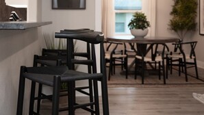 Moderni keittiö, jossa on baaritiski, ruokapöytä tuoleineen ja ruukkukasvi.