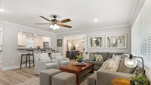 A modern living room with a sofa, ottomans, a coffee table, and a ceiling fan.