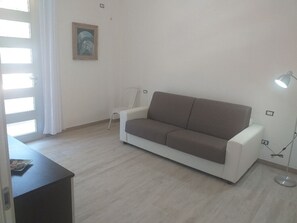 A room with a white sofa, a small table, a lamp, and a painting on the wall. - Da Vinci 86 - Apartment by the Sea. (Porto Cesareo)