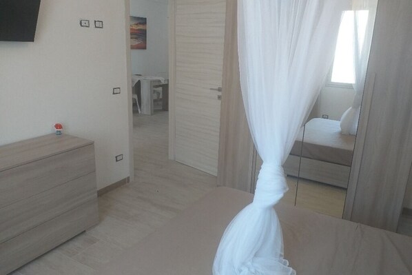 A bedroom with a bed, a bedside table, a dresser, and a TV mounted on the wall.