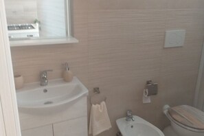 A bathroom with a sink, mirror, towel rack, toilet, and a window above the sink. - Da Vinci 86 - Apartment by the Sea. (Porto Cesareo)