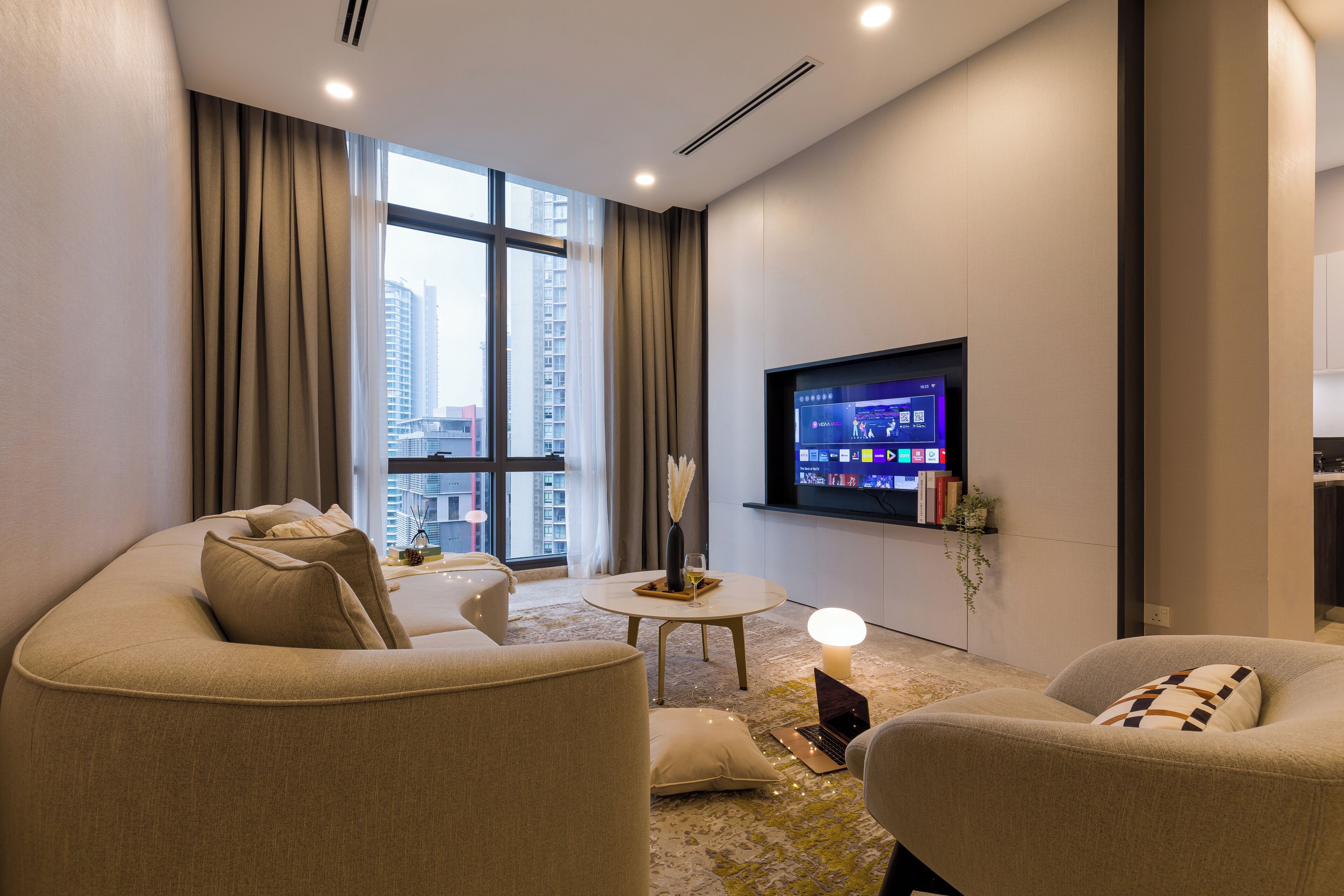 A modern hotel room with a large window, a flat-screen TV, a sofa, a small table, and a decorative candle.
