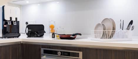 Una cocina moderna con cafetera integrada, tetera y sartén sobre la encimera.