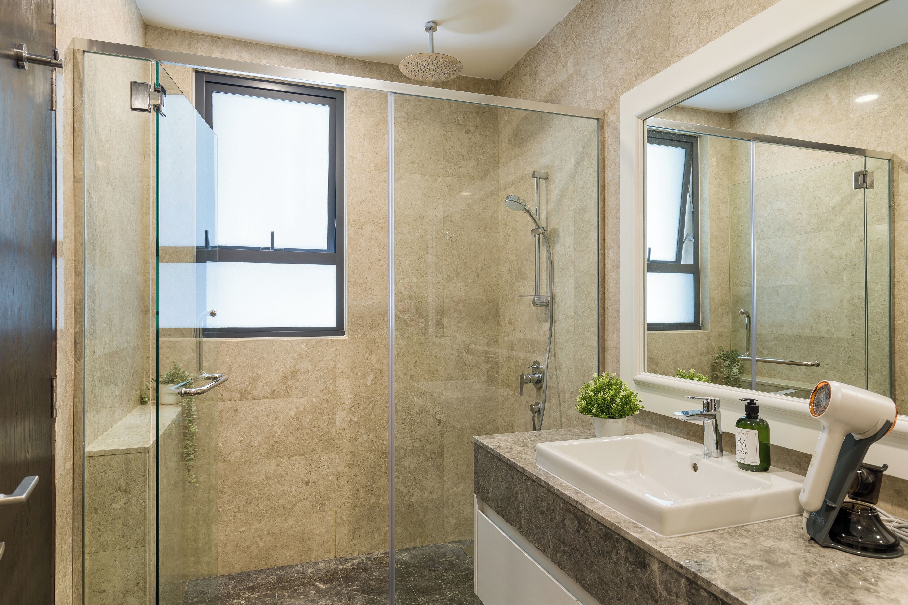 Een moderne badkamer met een douche in een glazen cabine, een grote spiegel en een marmeren aanrechtblad.