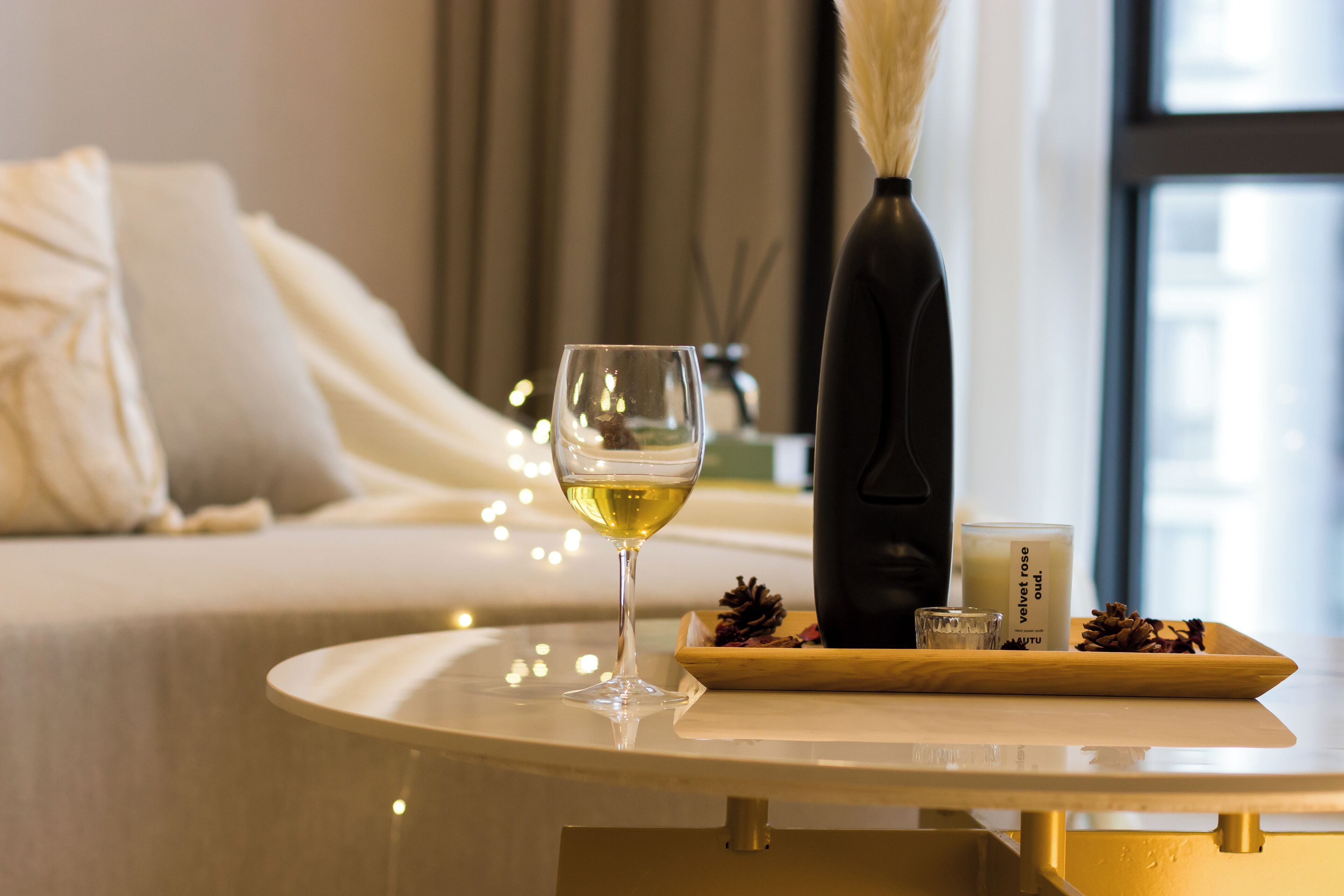 Una mesa ordenada con una copa de vino blanco, una vela y un florero decorativo con flores secas.